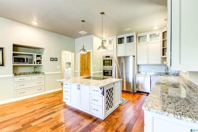 kitchen featuring light stone counters, stainless steel appliances, white cabinetry, light wood-type flooring, and glass insert cabinets