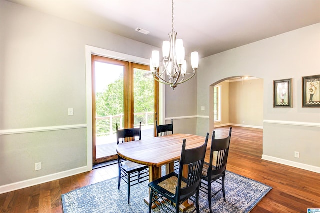 dining room with arched walkways, a chandelier, wood finished floors, visible vents, and baseboards