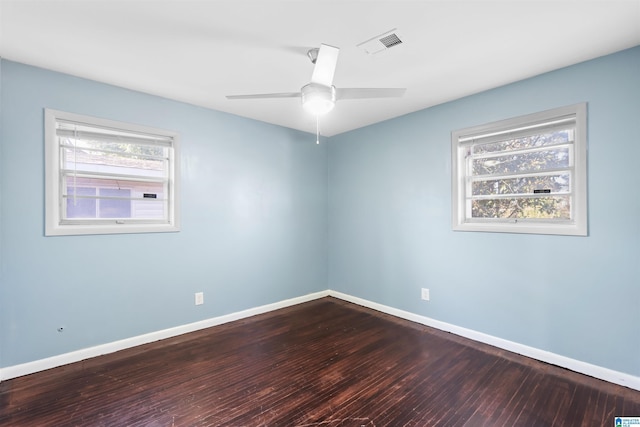 empty room featuring a healthy amount of sunlight, baseboards, visible vents, and dark wood-type flooring