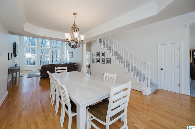 dining area with light wood finished floors, stairs, ornamental molding, and a raised ceiling