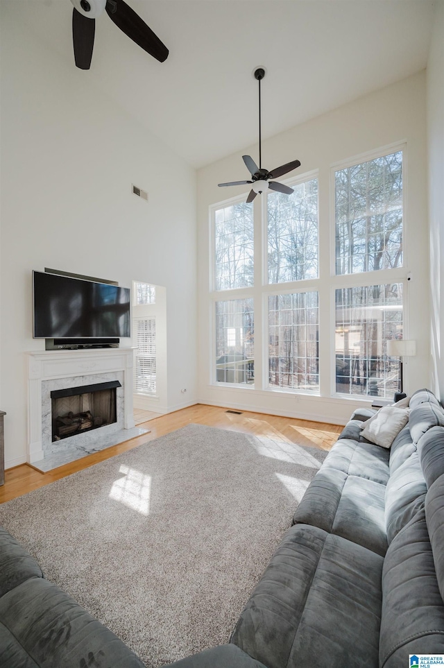 living room with a ceiling fan, a premium fireplace, a high ceiling, and wood finished floors