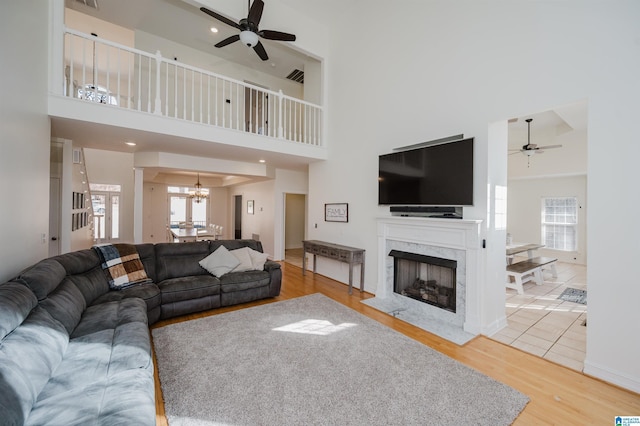 living area with baseboards, a towering ceiling, wood finished floors, a fireplace, and ceiling fan with notable chandelier