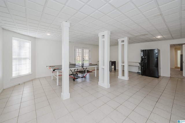 basement featuring french doors, light tile patterned floors, baseboards, and black fridge