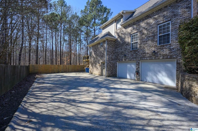 view of property exterior featuring a garage, brick siding, driveway, and fence