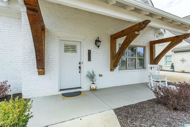 view of exterior entry featuring brick siding and a porch