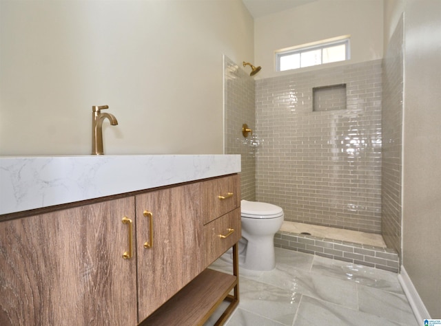 bathroom with toilet, marble finish floor, a tile shower, and vanity