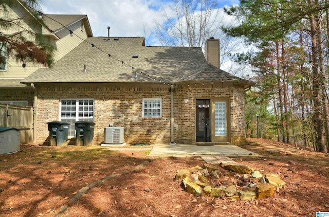 back of property with brick siding, a patio, a chimney, a shingled roof, and central AC unit