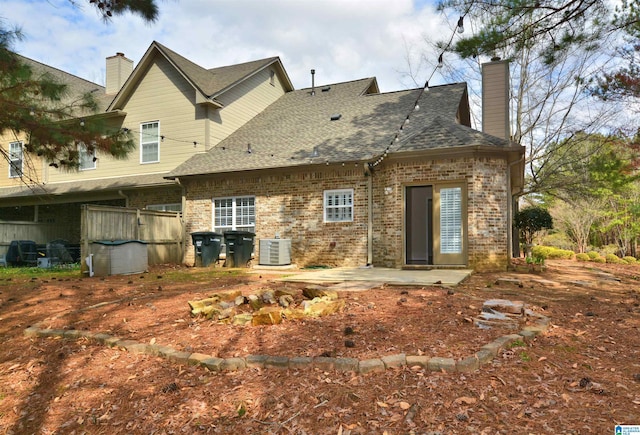 back of house with roof with shingles, brick siding, a patio, a chimney, and central air condition unit