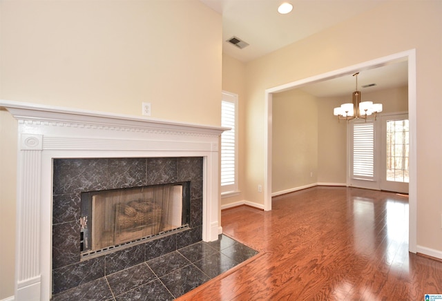 unfurnished living room with baseboards, visible vents, a tiled fireplace, wood finished floors, and a notable chandelier