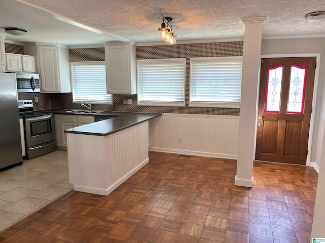 kitchen with stainless steel appliances, dark countertops, a sink, a peninsula, and ornate columns