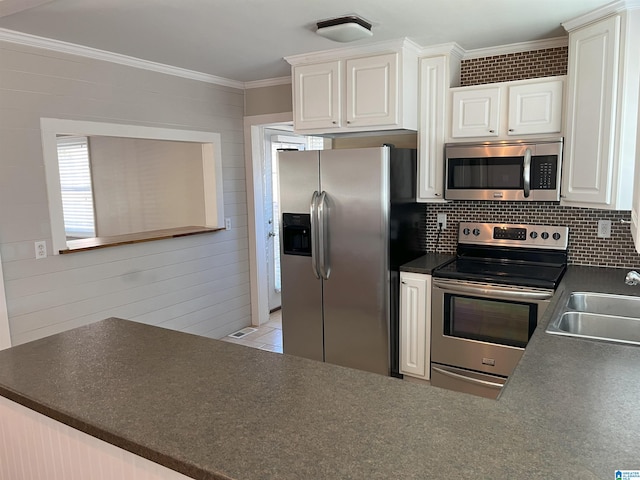 kitchen with appliances with stainless steel finishes, dark countertops, crown molding, and a sink