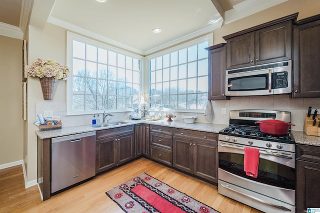 kitchen with dark brown cabinetry, stainless steel appliances, a sink, tasteful backsplash, and crown molding