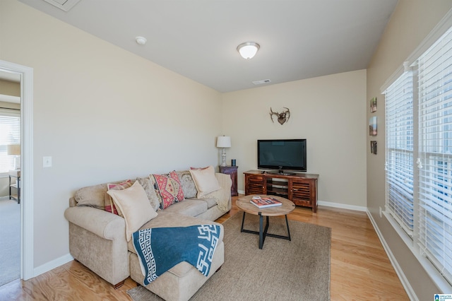 living room featuring visible vents, light wood-style flooring, and baseboards