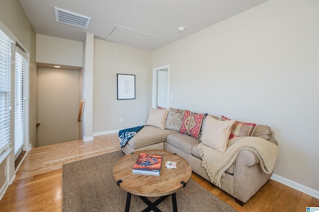 living area featuring attic access, visible vents, light wood-style floors, and baseboards