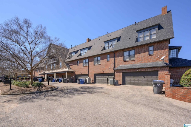 exterior space featuring a garage, central AC, brick siding, and a shingled roof