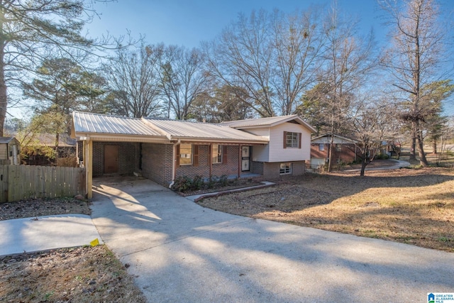 split level home featuring concrete driveway, metal roof, an attached carport, fence, and brick siding