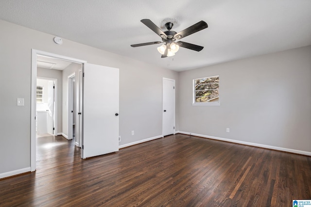 unfurnished bedroom with dark wood-type flooring, a ceiling fan, attic access, and baseboards