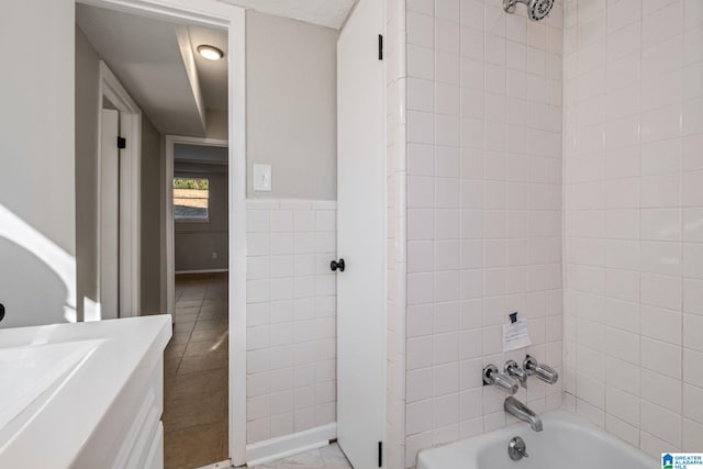 full bath with tile patterned flooring, a wainscoted wall, vanity, tile walls, and  shower combination