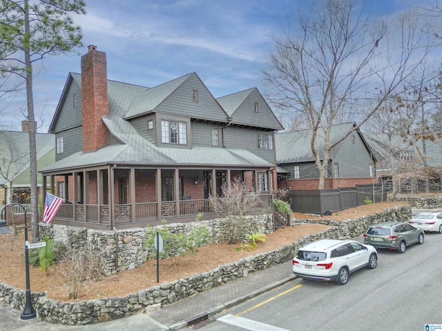 view of front facade featuring a chimney, fence, a porch, and brick siding