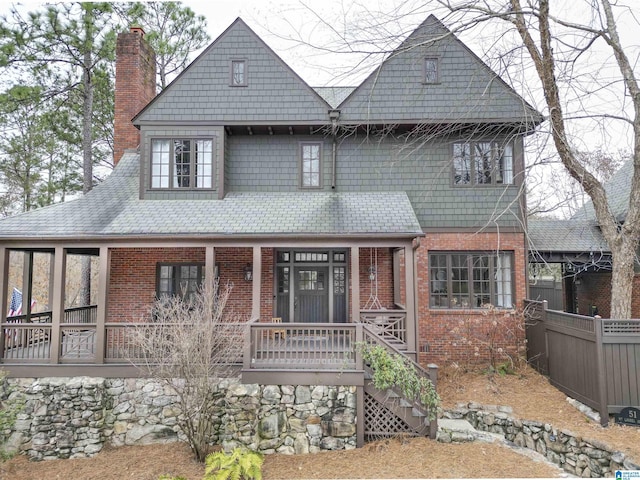 view of front of home featuring brick siding, a chimney, covered porch, fence, and stairs