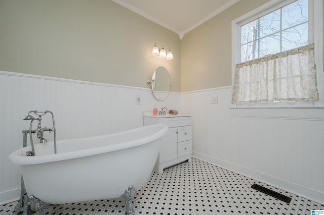 bathroom with a wainscoted wall, vanity, visible vents, a freestanding bath, and crown molding