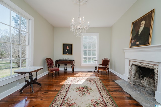 living area featuring dark wood-type flooring, a fireplace, an inviting chandelier, and baseboards