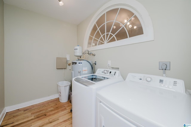 clothes washing area featuring electric water heater, light wood-style flooring, laundry area, baseboards, and washing machine and clothes dryer