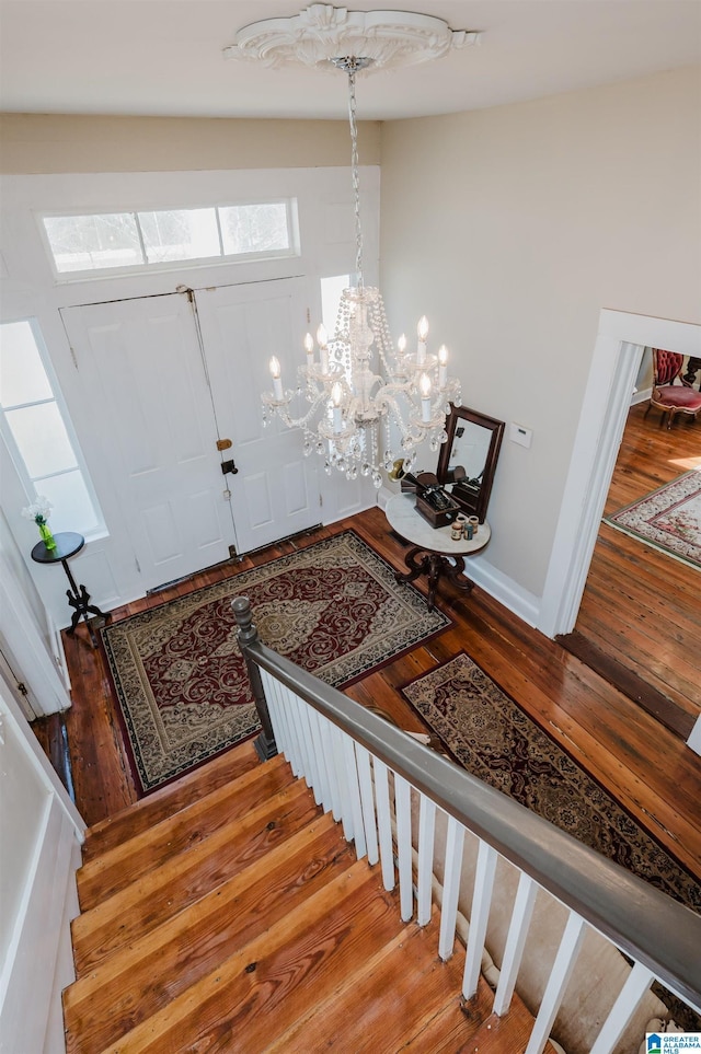 entryway featuring stairs, a notable chandelier, wood finished floors, and baseboards