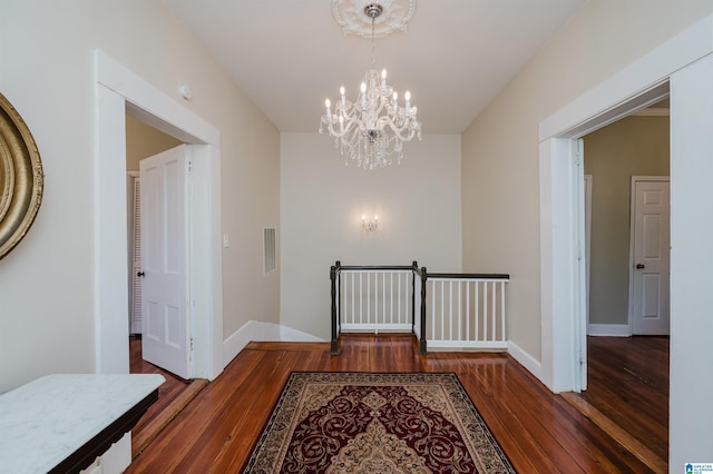 hallway featuring visible vents, baseboards, wood finished floors, an inviting chandelier, and an upstairs landing