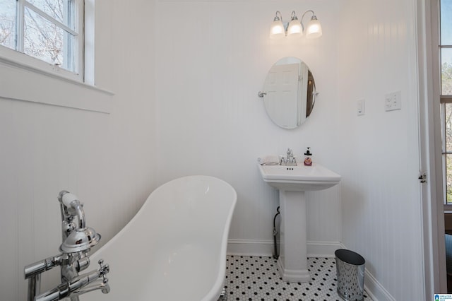 full bathroom with a soaking tub, a sink, baseboards, and tile patterned floors