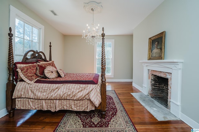 bedroom featuring a fireplace, a notable chandelier, visible vents, wood finished floors, and baseboards