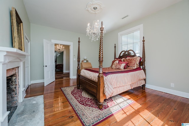 bedroom with baseboards, visible vents, hardwood / wood-style flooring, a fireplace, and a notable chandelier