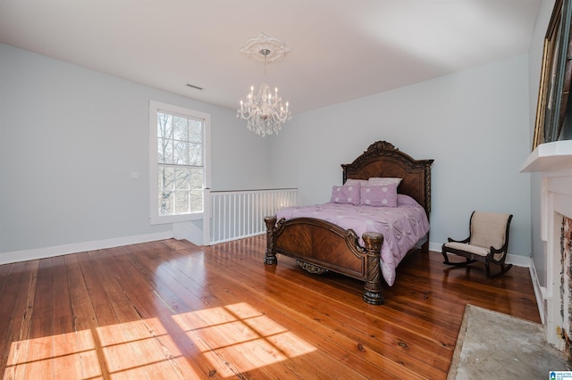 bedroom featuring a notable chandelier, a fireplace with flush hearth, baseboards, and hardwood / wood-style floors