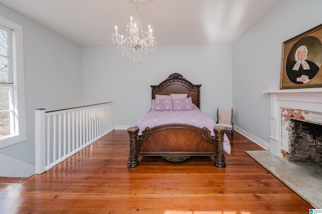 bedroom with a fireplace with flush hearth, multiple windows, a notable chandelier, and wood finished floors