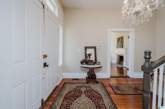 foyer entrance with dark wood-style floors, a fireplace with flush hearth, baseboards, and a notable chandelier