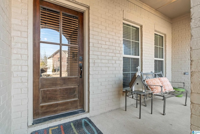 view of exterior entry featuring a porch and brick siding