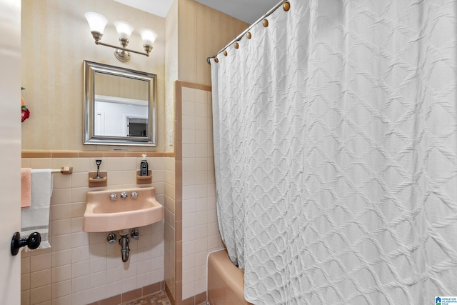 bathroom with a sink, shower / bath combo with shower curtain, tile walls, and wainscoting