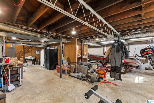 unfinished basement featuring stairs and black fridge