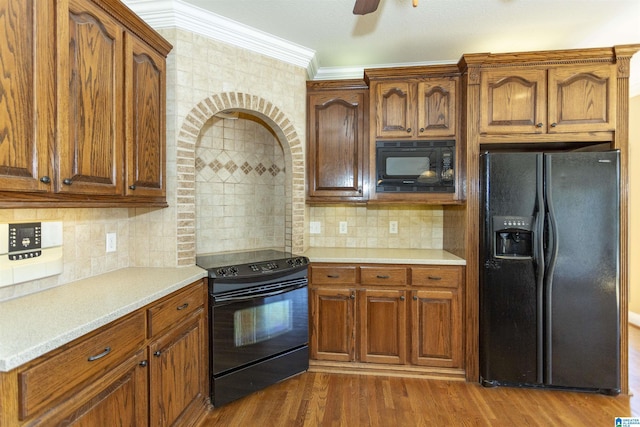 kitchen featuring dark wood-type flooring, black appliances, tasteful backsplash, crown molding, and light countertops