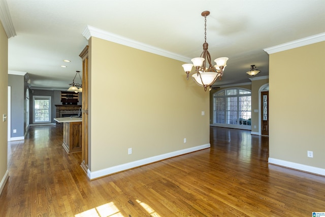 unfurnished room with a notable chandelier, crown molding, baseboards, and wood finished floors