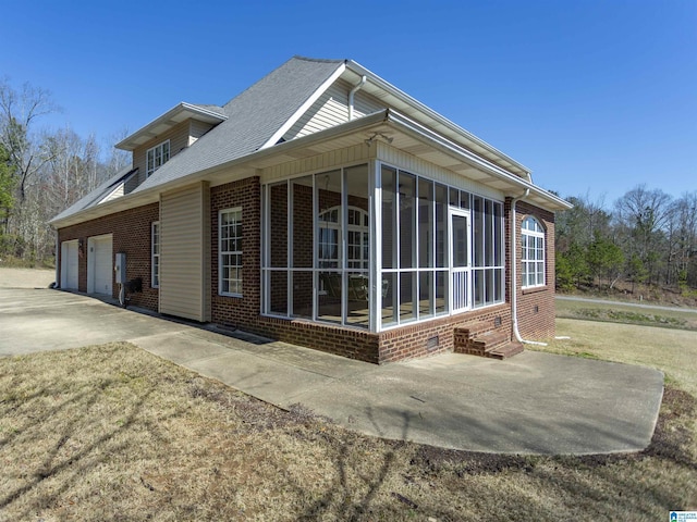 view of home's exterior with driveway, a sunroom, a shingled roof, a garage, and brick siding