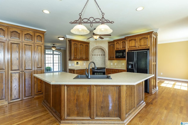 kitchen with black appliances, crown molding, light countertops, and a sink