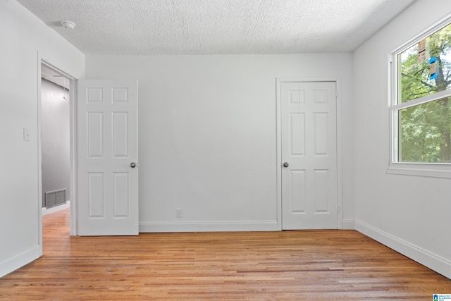 spare room with light wood-type flooring, visible vents, a textured ceiling, and baseboards