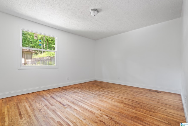 empty room with light wood finished floors, visible vents, baseboards, and a textured ceiling