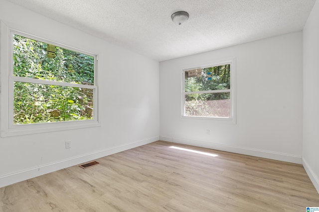 spare room with a textured ceiling, light wood-style flooring, and visible vents