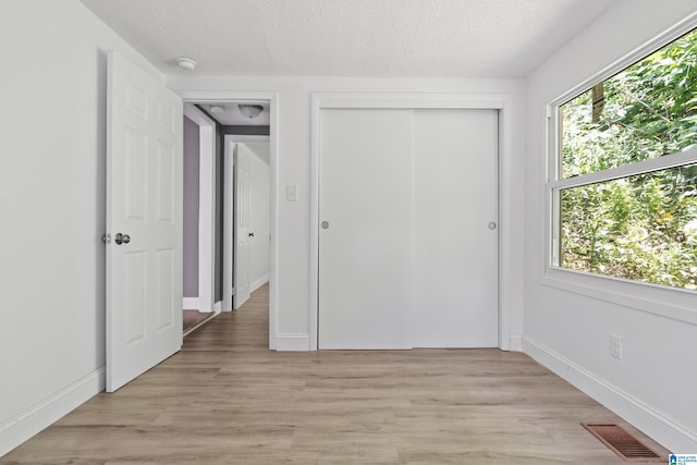 unfurnished bedroom with light wood-type flooring, visible vents, a textured ceiling, and multiple windows