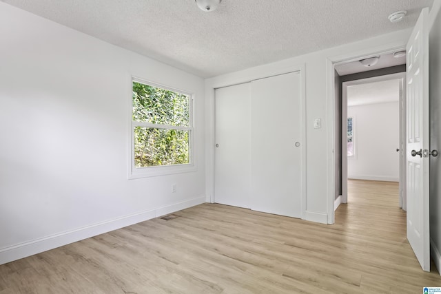 unfurnished bedroom with light wood-type flooring, a closet, a textured ceiling, and baseboards