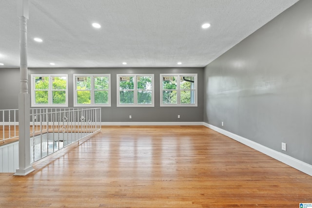 empty room featuring a textured ceiling, light wood-style flooring, recessed lighting, baseboards, and decorative columns