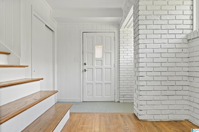 entrance foyer with light wood-type flooring, wood walls, brick wall, and stairs