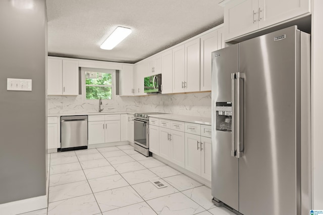 kitchen with marble finish floor, light countertops, backsplash, appliances with stainless steel finishes, and white cabinetry